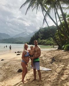 a man and woman are standing on the beach with a baby in their arms,