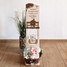 an arrangement of flowers in a basket on a wooden floor next to a sign with a couple sitting on a bench