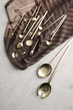 gold spoons and forks laid out on top of a cloth with a striped napkin