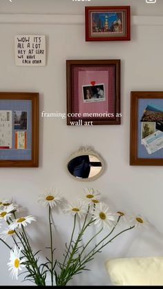 a vase filled with white daisies sitting next to pictures on the wall above it