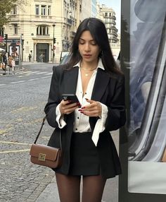 a woman standing next to a bus looking at her cell phone and holding a purse