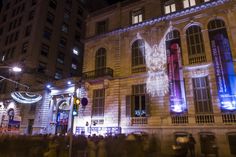 people walking on the street in front of a building with lights and banners projected on it