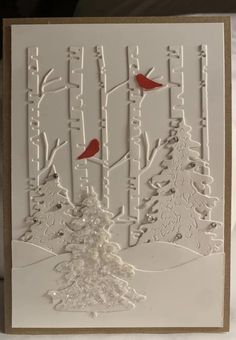 a white card with red birds sitting on top of trees and snow covered ground in the background