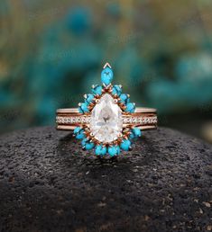 a ring with an aqua and white stone surrounded by diamonds on top of a rock