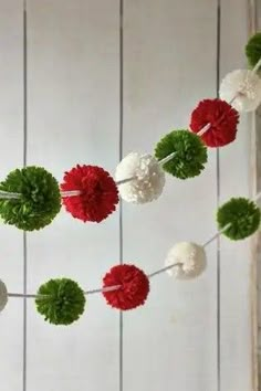 red, white and green pom - poms are hanging from a string on the wall