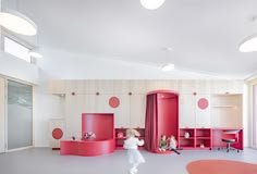 a child's playroom with pink furniture and toys on the floor, while a woman walks by