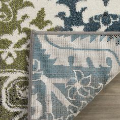 an area rug with blue and green designs on the ground next to a wooden floor