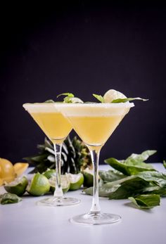 two glasses filled with drinks sitting on top of a table next to leaves and flowers