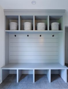 a white bench with baskets on the top and shelves above it in a room that has gray tile flooring