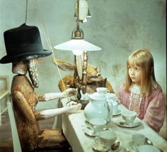 two children are sitting at a table with an alien lamp in the corner and one child is holding a teapot