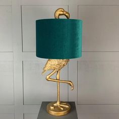 a gold flamingo lamp with a teal shade on it's head and legs