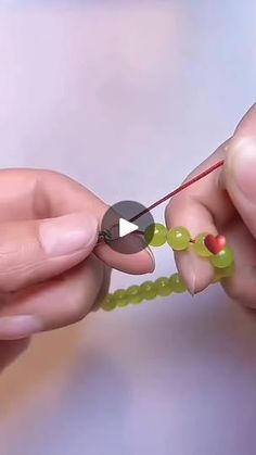 two hands are holding some beads and knitting them together with scissors, string and thread