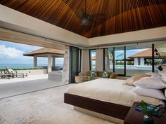 a bedroom with a large bed sitting under a wooden ceiling next to an ocean view