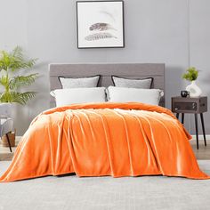 an orange blanket on top of a bed in a room with grey walls and furniture