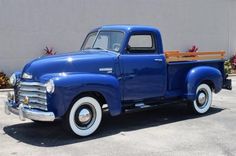 an old blue pick up truck parked in a parking lot next to a cement wall