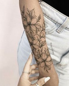 a woman's arm with flowers on it and a hand holding the arm tattoo