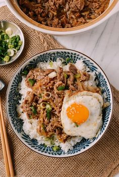 two bowls filled with rice and meat next to chopsticks on a table top