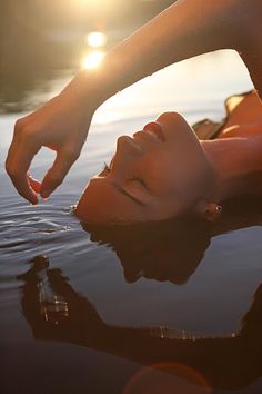 a woman laying on top of a body of water next to the sun shining down