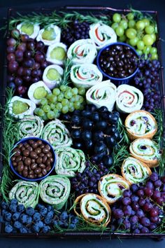 a platter filled with grapes, olives, rolls and other food on top of it