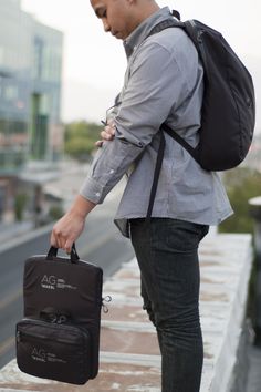 a man with a backpack and briefcase is standing on a ledge looking down at his cell phone