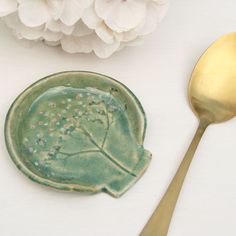 a green plate with a tree on it next to a gold spoon and white flowers