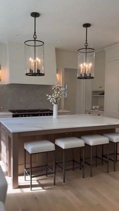 a kitchen island with four stools in front of it and lights hanging from the ceiling