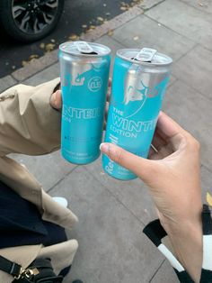 two people holding up cans of water on the sidewalk