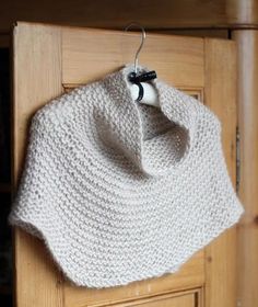 a white knitted shawl hanging on a wooden door with a black bow tie