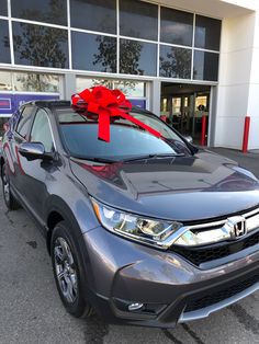 a gray honda car with a red bow on it's hood in front of a building