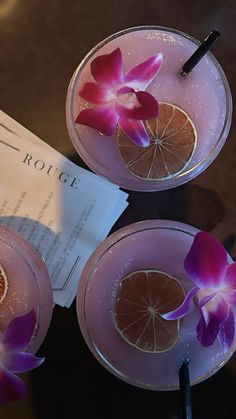 two glasses filled with drinks and garnished with flowers on the rim, sitting on a table