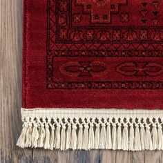 a red rug with tassels on top of it sitting on a wooden floor