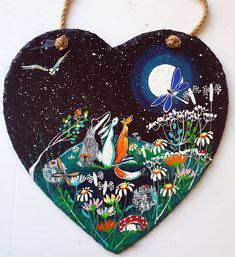 a painted heart hanging on a wall with flowers and birds in the night sky above it