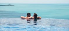 two people are sitting in the pool looking out at the water and one person is laying on his back