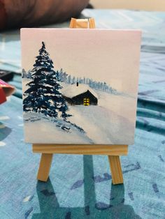 a small easel sitting on top of a table covered in snow next to a painting