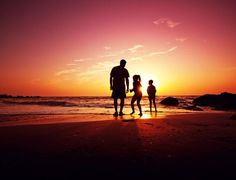 a family walking on the beach at sunset