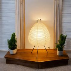 a white lamp sitting on top of a wooden table next to two potted plants