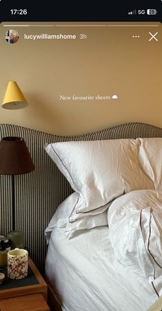 a bed with white sheets and pillows next to a lamp on a nightstand in a bedroom