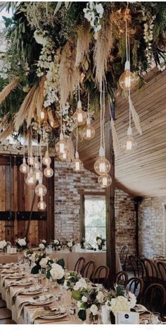 a long table with many place settings and flowers hanging from the ceiling in an old barn