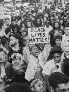 a large group of people holding signs and standing in the middle of a crowd with their hands up