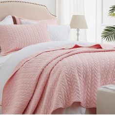 a bed with pink comforter and pillows in a bedroom next to a plant on the floor