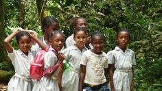 a group of young children standing next to each other in front of trees and bushes