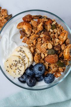 a glass bowl filled with granola, yogurt and blueberries on top of a table