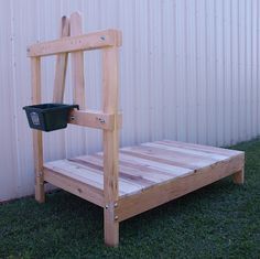 a wooden bed frame sitting on top of grass next to a white building with a bucket in it