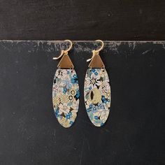 two pairs of blue and white flowers are hanging from gold earwires on a black surface