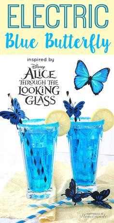 two glasses filled with blue liquid sitting on top of a table next to a butterfly