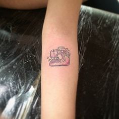 a small camera tattoo on the left forearm and right arm, is shown in pink ink