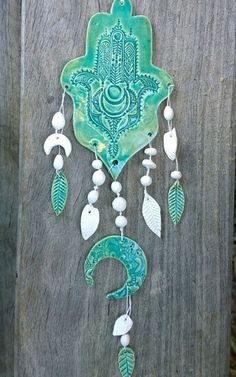 a green and white wall hanging on a wooden fence with beads, shells and leaves