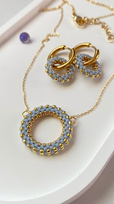 two pieces of jewelry sitting on top of a white table next to a blue beaded necklace