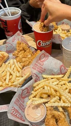 people are eating chicken and french fries at a table with cups of sodas on it