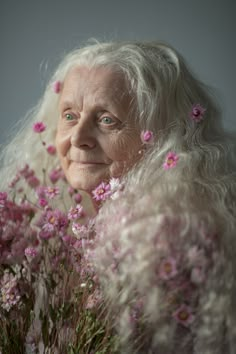 an older woman with white hair and blue eyes is surrounded by pink flowers